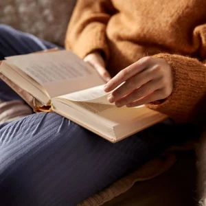 Person in a cozy sweater turning pages of a book while learning adverbs in arabic