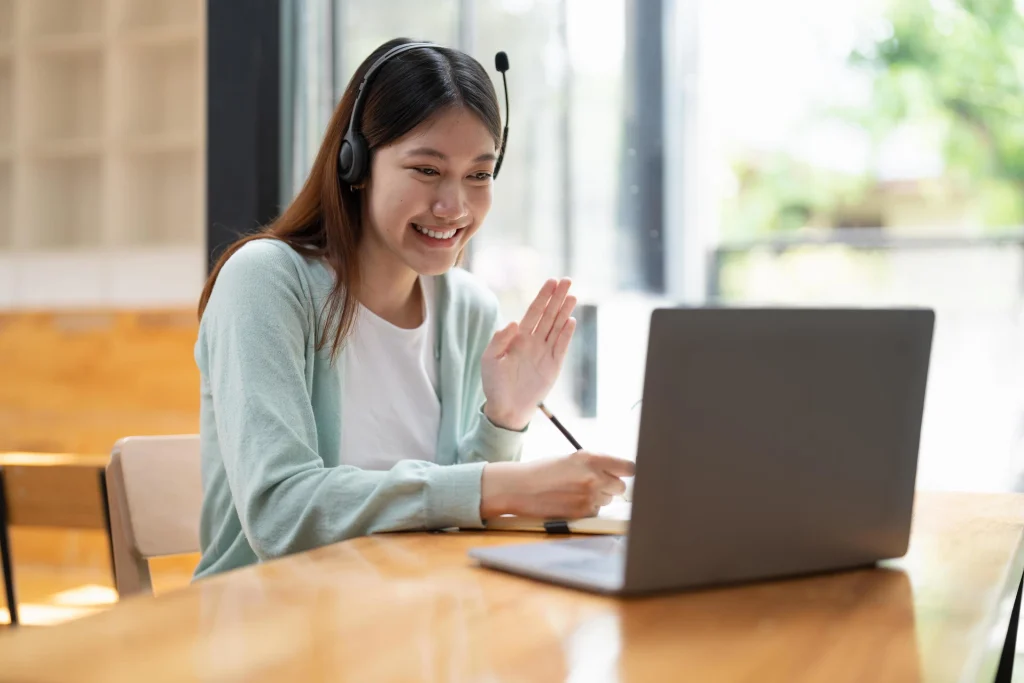 Woman wearing a headset waving and smiling during an online class on her laptop